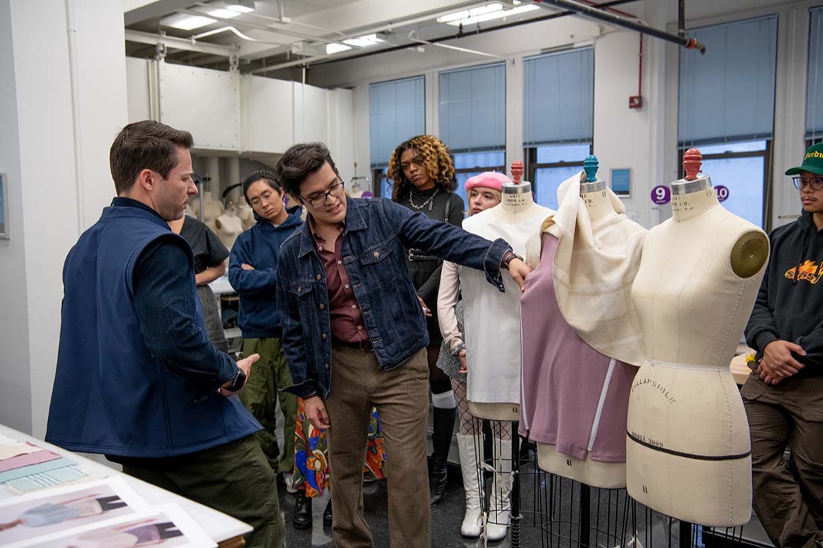 Designers reviewing garments on dress forms with a group in a fitting studio