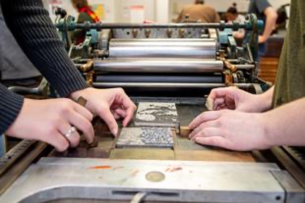 Two makers' hands setting type on a letterpress bed