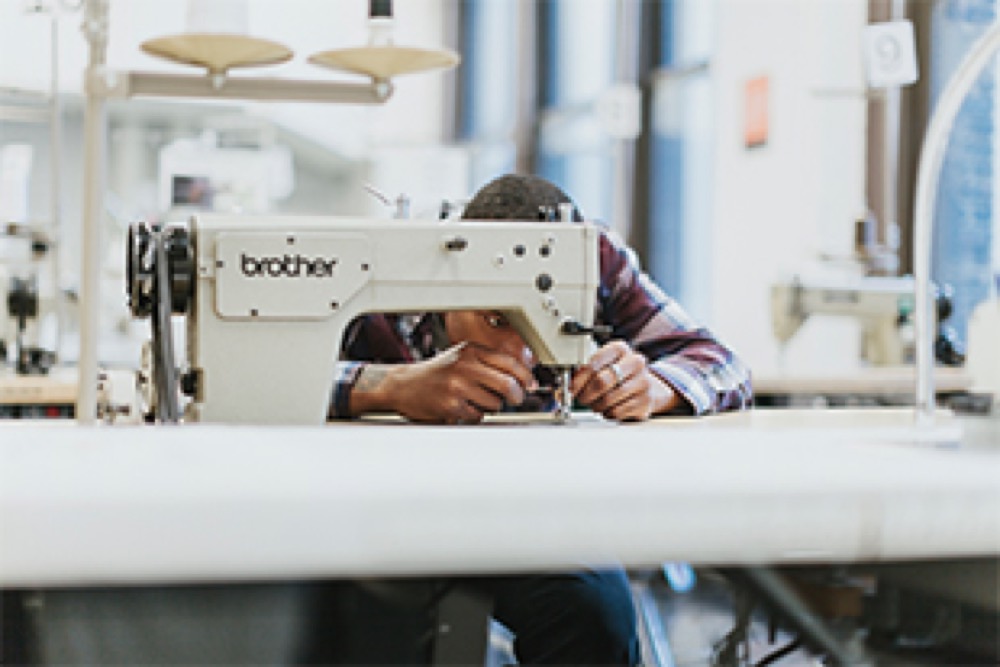 Maker leaning into a Brother industrial sewing machine in a textile studio