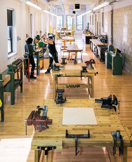 Long institutional wood shop lined with workbenches and vises