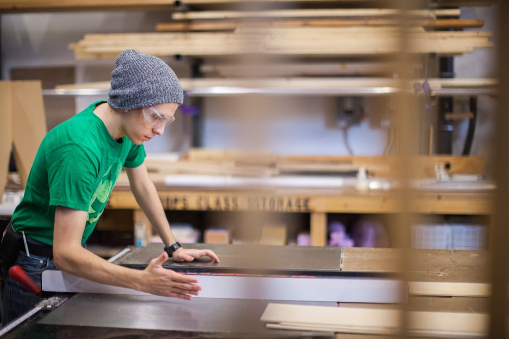Maker measuring a panel at a table saw in a wood shop